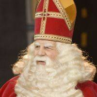 Een man met een lange witte baard draagt een rode mijter en een rood gewaad met gouden versieringen